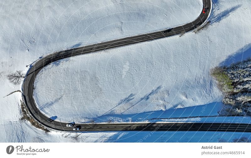 Luftaufnahme mit einer Drohne von einer verschneiten Landschaft mit einer kurvigen Straße mit Autos luftaufnahme drohnenfoto landschaft winter schnee straße