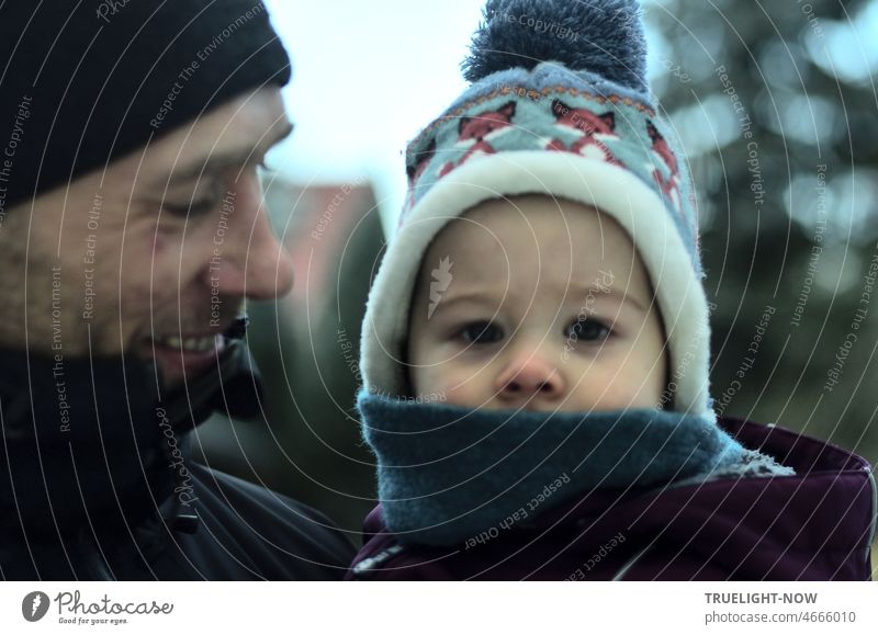 Loving father holding his 1 year old son in his arms outside in the cold, looking very attentive and serious at the camera Baby Child Father at the same time