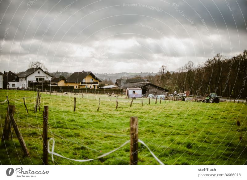 Rural settlement under dark cloudy sky houses Meadow Fence Fence post Pole Fences Forest Sky Clouds Storm clouds Thunder and lightning stormy atmosphere