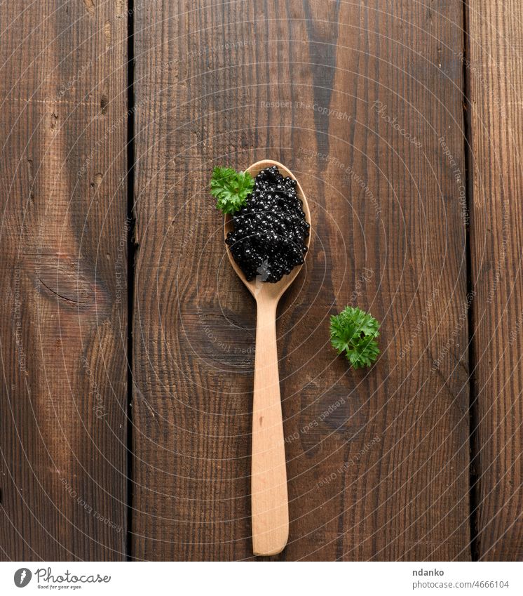 fresh grainy black paddlefish caviar in brown wooden spoon on a black background, top view green appetizer breakfast caviare closeup delicacy delicatessen