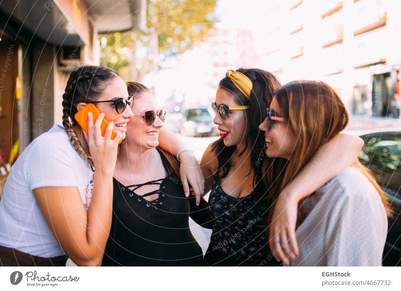 Group of four young females friends chatting with mobile phone a sunny day in the city, carefree cheerful city life enjoy enjoyment fashion fashionable