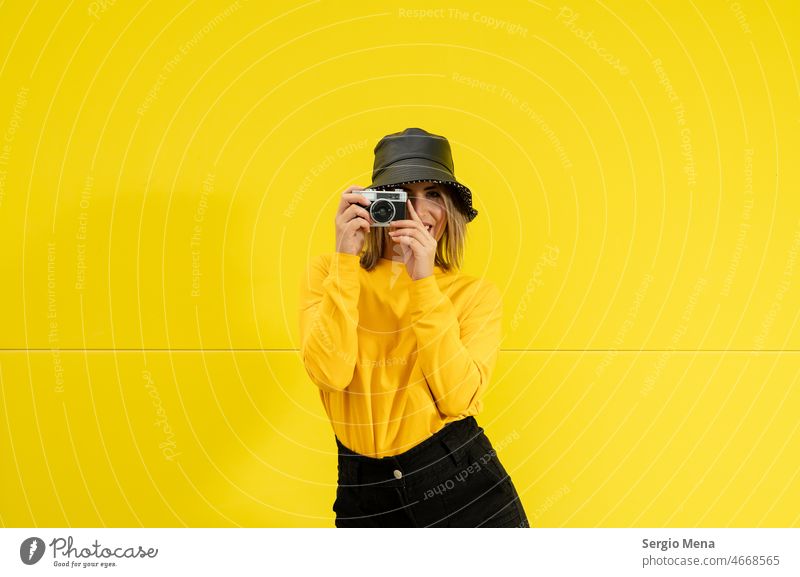 closeup of a young caucasian woman with a black hat , on a yellow background holding an old photo camera portrait beautiful female people person adult looking