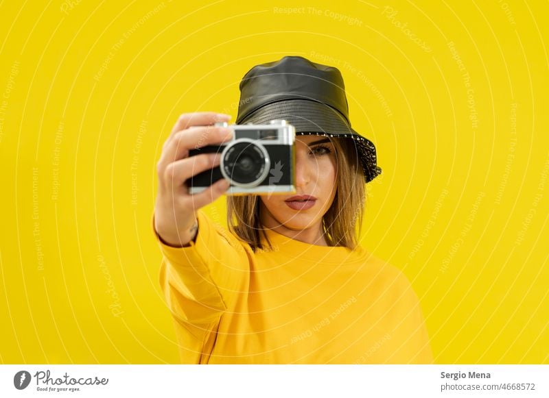 closeup of a young caucasian woman with a black hat , on a yellow background holding an old photo camera person female beautiful adult people portrait