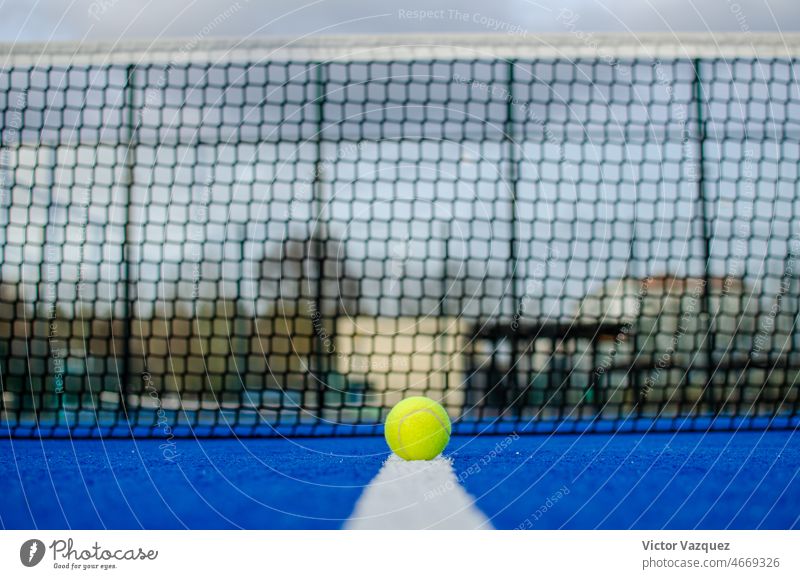 Selective focus. Ground level view of a ball on the line of a blue paddle tennis court with the net out of focus in the background. activity athletics