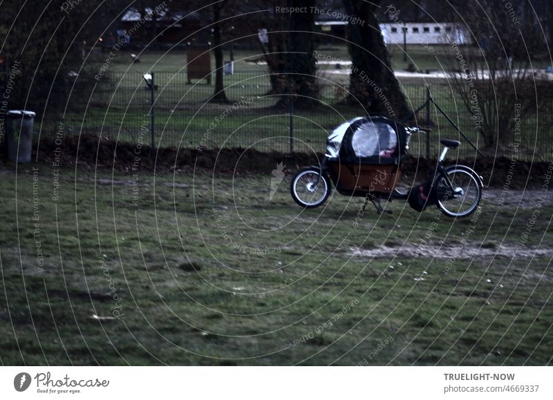 A cargo bike, a modern bicycle children's rickshaw with transparent protective hood for trips in wind and weather parked on a lawn at the Havel lido in Babelsberg