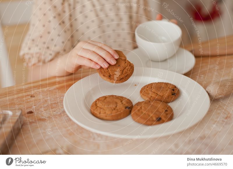 Unrecognizable young girl eating cookies from white plate in the kitchen while baking and drinking tea. Kid eating dessert. closeup baked food treat style