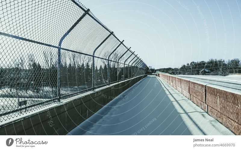 Sidewalk over the highway covered in snow with chain-link fence and concrete barricade horizon diminishing perspective color bridge street walking city life