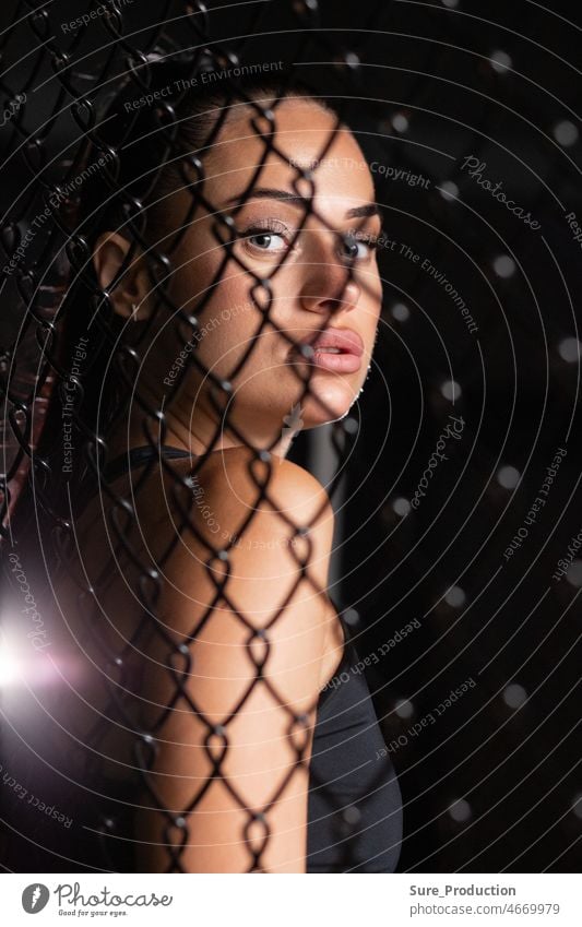Woman fighter looks at you through the net A human in a dark cage behind the light breaks through. mesh body sport champion confidence sexy slim sportswear