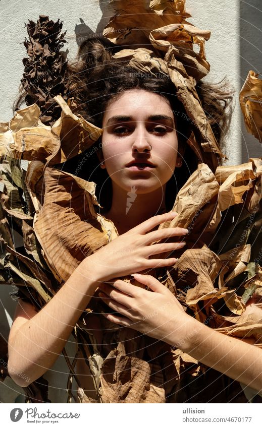 Portrait of young sexy brunette woman covered by leaves of dry, withered banana tree, accuses the world for climate change portrait girl decorative lying shadow