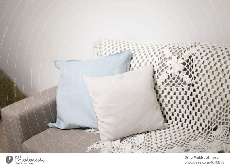 Pillows on a couch near white wall. Light blue and gray pillows and knitted blanket on a beige sofa in scandinavian minimalist style apartment interior. Home decor with copy space on top.