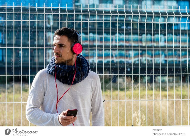 Young man listening music by headphones while holding a mobile phone outdoor smartphone city person lifestyle urban street communication earphones adult