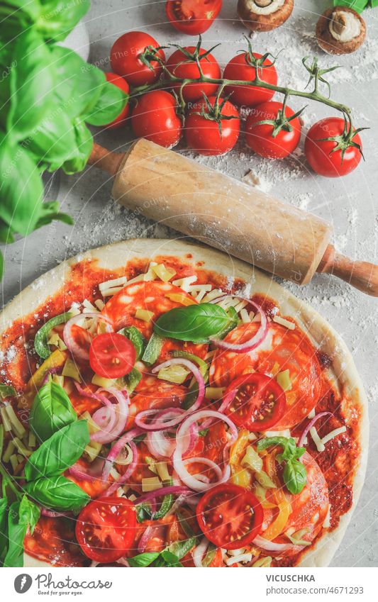 Close-up of homemade pizza with tomatoes, salami, onion and basil at kitchen table italian food close-up flour wooden rolling pin ingredients cooking