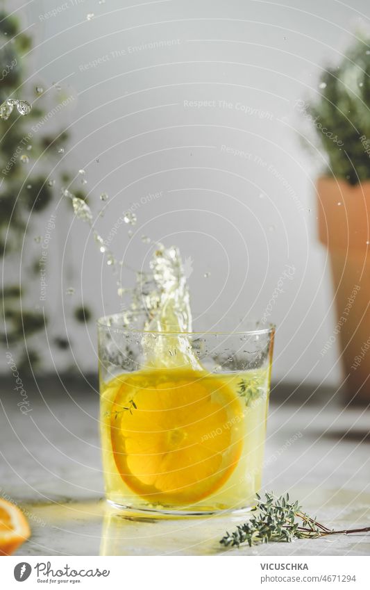 Homemade splashing orange lemonade in glass with thyme on kitchen table homemade wall plant background refreshing drink summer fruit front view beverage