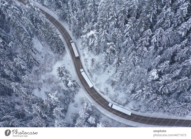 Convoy of Trucks Moving During Snowfall on a Winding Curving Winter Mountain Road truck convoy road curving winding landscape aerial winter drive forest snow