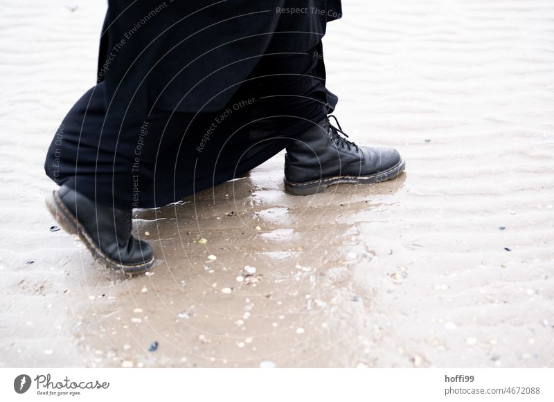 Black boots with long coat stride through mudflats at low tide Steps Mud flats Water Puddle black boots Black coat minimalism Boots Stride Going moving