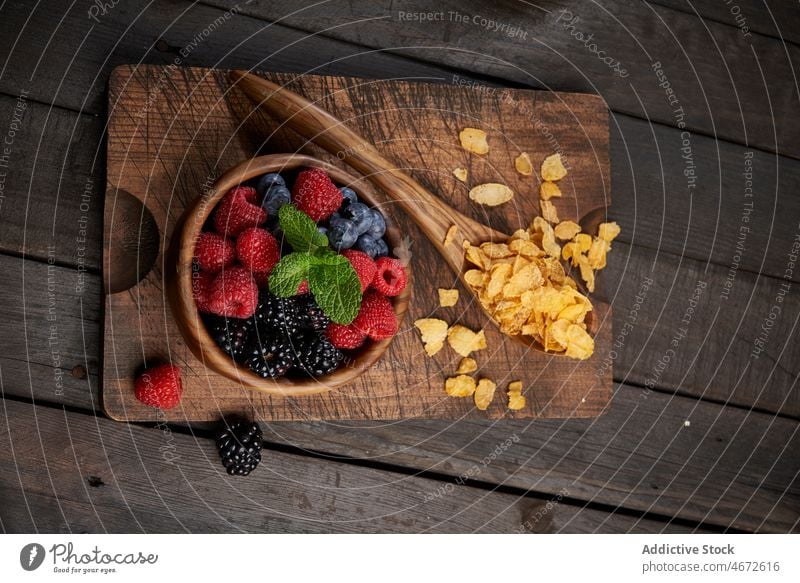 Cornflakes near bowl of berries cornflake sweet breakfast cereal berry healthy food vitamin morning kitchen flavor tasty cutting board table delicious nutrition