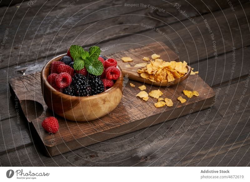 Cornflakes near bowl of berries cornflake sweet breakfast cereal berry healthy food vitamin morning kitchen flavor tasty cutting board table delicious nutrition