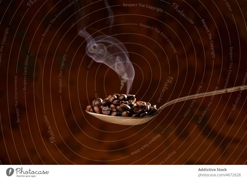 Spoon full of heated coffee beans on brown background roast spoon heap pile aroma smoke ingredient energy natural caffeine grain product delicious organic