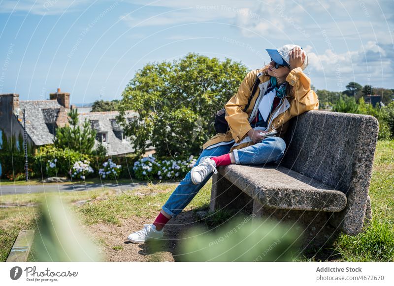 Woman on bench in town woman building suburb house travel traveler neighborhood street rest female residential plant stone headwear vacation casual france