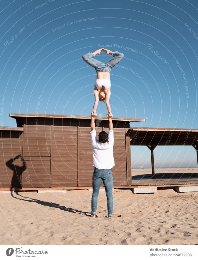 Anonymous couple doing handstand on beach sport hand to hand acrobat acrobatic exercise embankment practice training sporty flexible fit woman waterfront coast