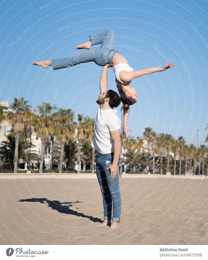 Man holding woman on outstretched arm on beach couple sport acrobat acrobatic exercise embankment practice waterfront sporty flexible fit figure coast shore