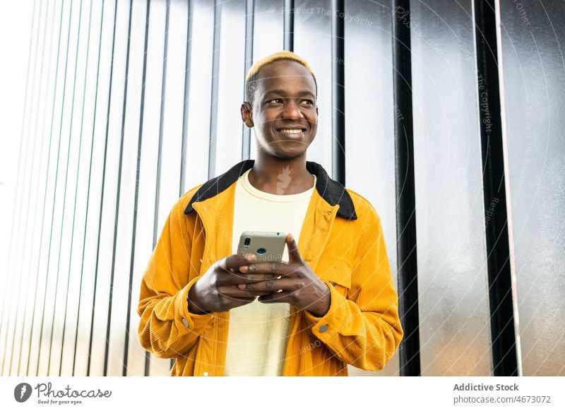 Cheerful black man browsing smartphone online text message style wall chat digital street appearance fashion dyed hair modern young casual short hair town male
