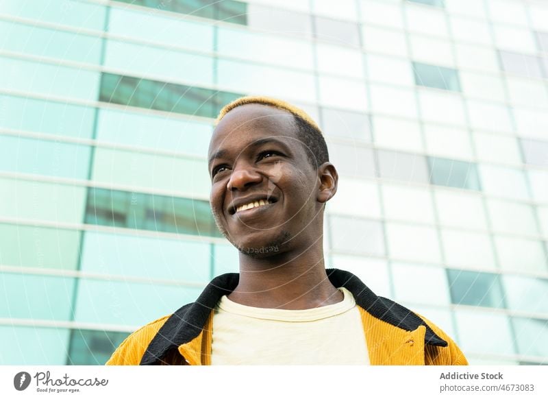 Smiling black man near multistory building style trendy smile urban street style glad appearance city dyed hair delight happy modern young casual short hair