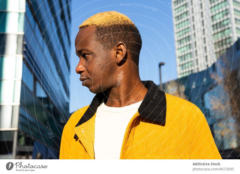Black man near multistory building style trendy urban street style appearance city dyed hair modern young casual short hair wall dreamy pensive confident