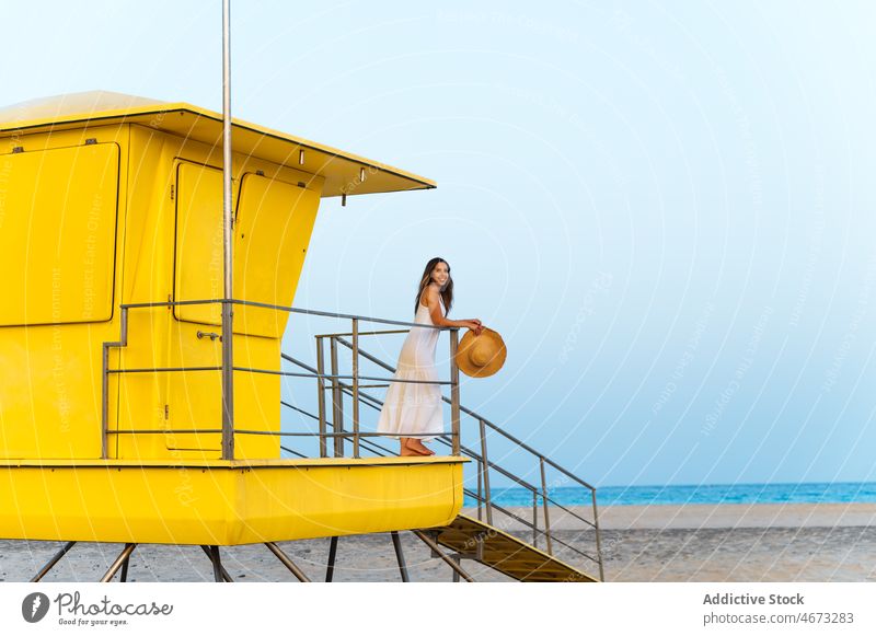 Woman standing near lifeguard hut woman beach shore alone contemplate travel sand coast yellow tower building sea female observe seashore seaside cabin color
