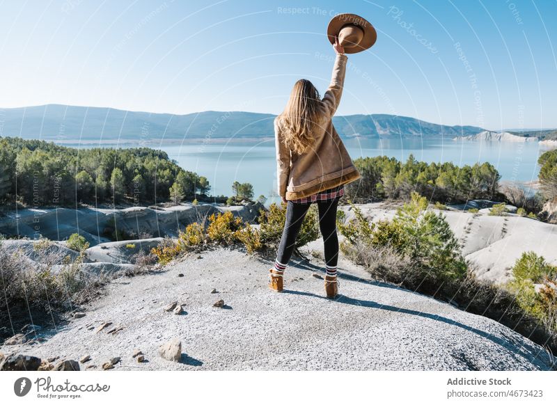 Woman standing on boulder and admiring nature woman lake admire scenery shore rock freedom contemplate environment raised arm female mountain highland outerwear