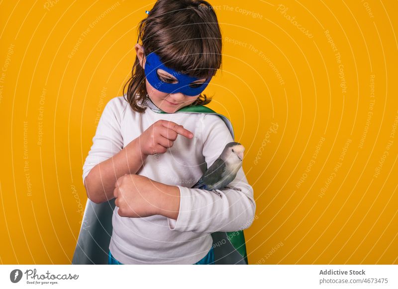 Child in superhero costume with parrot child girl bird point indicate studio portrait model show kid courage brave power ambition mask individuality pet