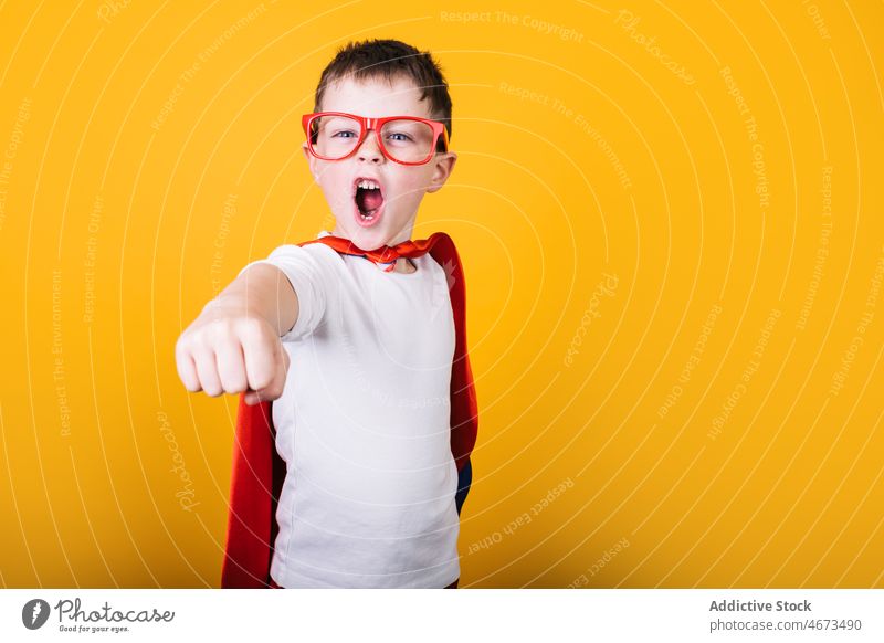 Playful boy in superhero uniform pretending to fly child flight clench fist scream costume portrait studio power kid courage confident cape brave strong