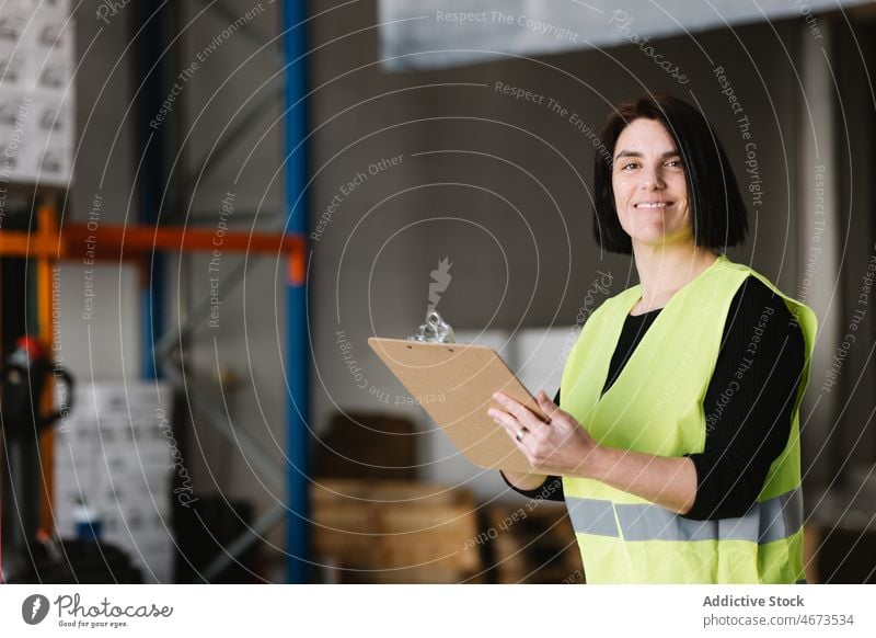 Happy woman taking notes while checking supplies warehouse take note smile write storage work Hi-Vis storehouse happy labourer examine female vest professional