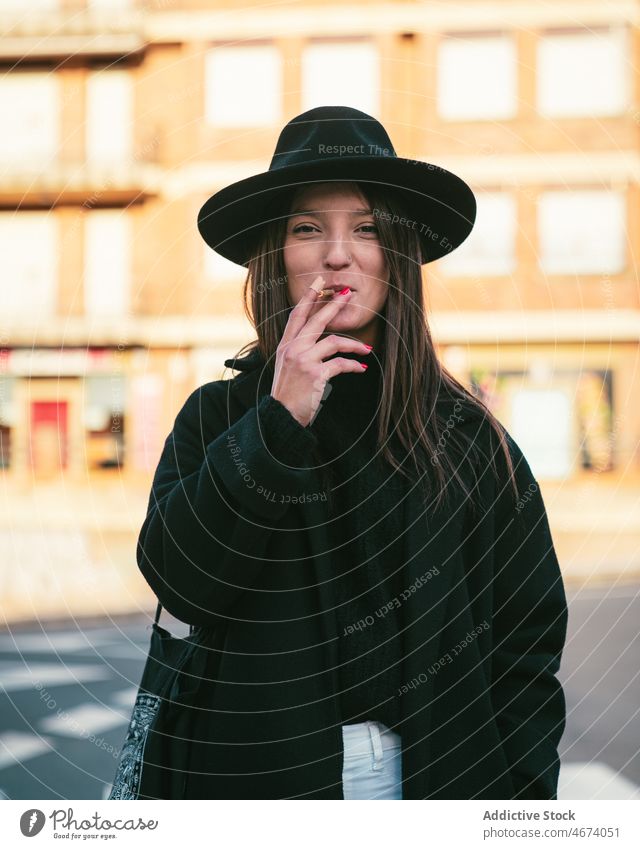 Stylish woman smoking on street smoke smoker cigarette habit style road nicotine city tobacco addict female district lady hat building house content town light