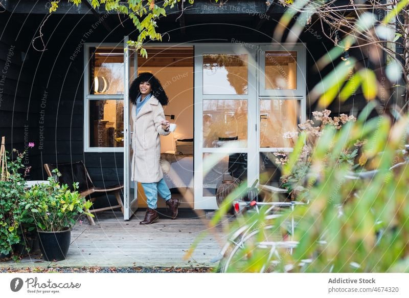 Happy black woman standing in doorway of house home walking out warm clothes coat outerwear urban coffee cup beverage tea female african american woman