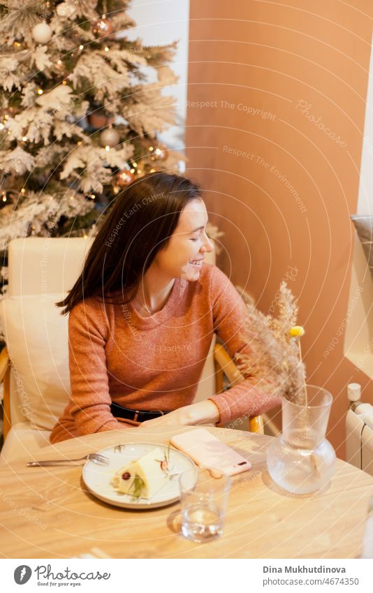 Young woman sitting at a table in cafe with christmas tree lights behind her, eating a cake on Valentine's day. Young woman at cafe candid lifestyle beautiful