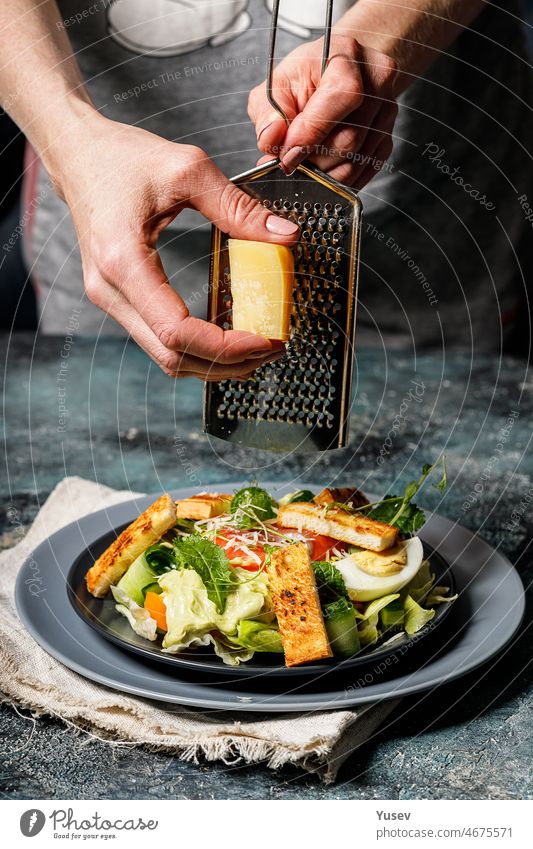 Woman hands grating cheese in salad with salmon, vegetables and croutons. Mediterranean Kitchen. Healthy diet. Vertical shot woman smoked mediterranean kitchen