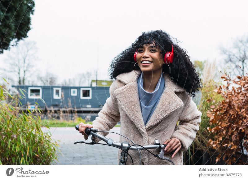 Cheerful black woman in headphones with bicycle using music listen bike chill relax city female african american woman street smile walk stroll positive rest