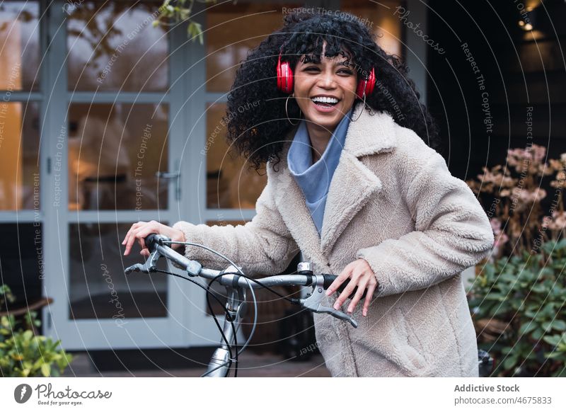 Cheerful black woman in headphones with bicycle using music laugh listen bike chill relax city female african american woman street smile walk house stroll