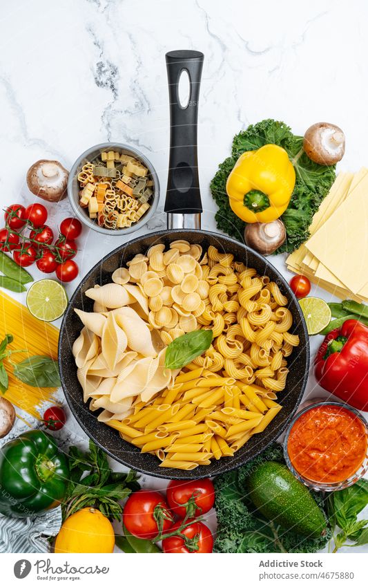 Frying pan with assorted raw pasta amidst vegetables various frying pan uncooked kitchen food recipe culinary cuisine ingredient product prepare bell pepper