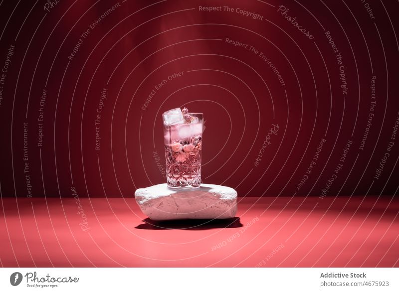 Gin tonic with ice on red background cocktail pink gin alcohol beverage booze glass aperitif studio cold cube drink refreshment frozen liquid ingredient serve