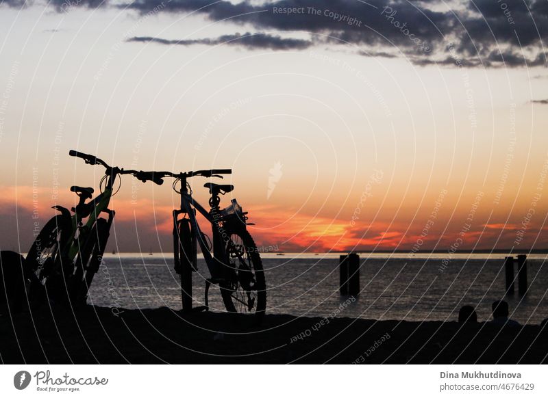 Silhouettes of bicycles parked at the beach at sunset. Bikes by the seaside during colorful sunset. Healthy lifestyle and eco transportation. outdoor activity