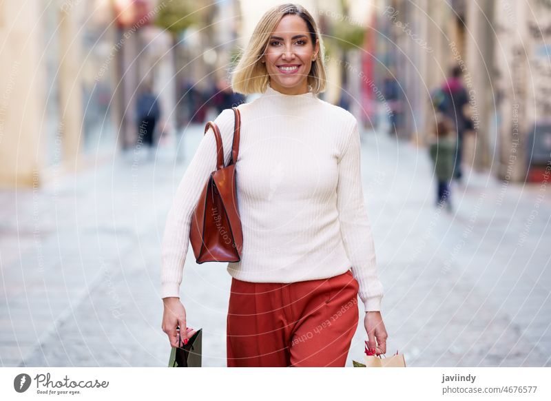 Smiling woman with shopping bags walking on street shopper carry carefree consumerism goods retail modern purchase female happy paper bag positive glad city