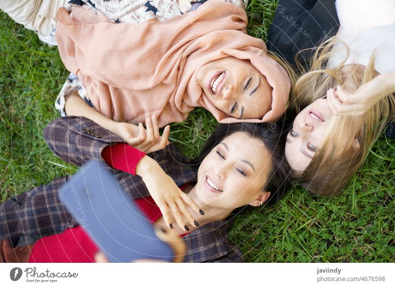 Multiracial women taking selfie together in park friend friendship self portrait lawn photography capture bonding memory smartphone multiracial multiethnic