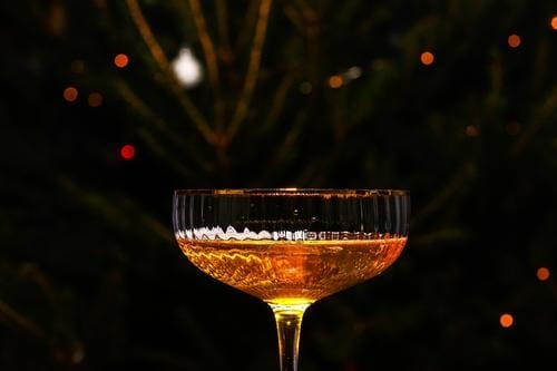 Beautiful glass of champagne against bokeh lights background with a decorated Christmas tree. Happy New Year 2022. Christmas and New Year holidays background, winter season.
