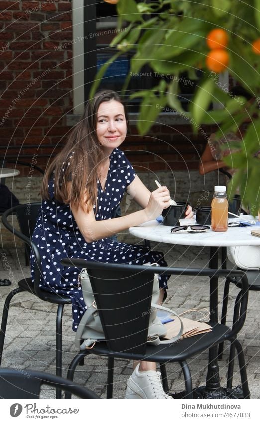 Candid portrait of woman eating at cafe terrace, smiling. Authentic lifestyle of millennial woman in summer in the city. Terrace beautiful relax coffee happy
