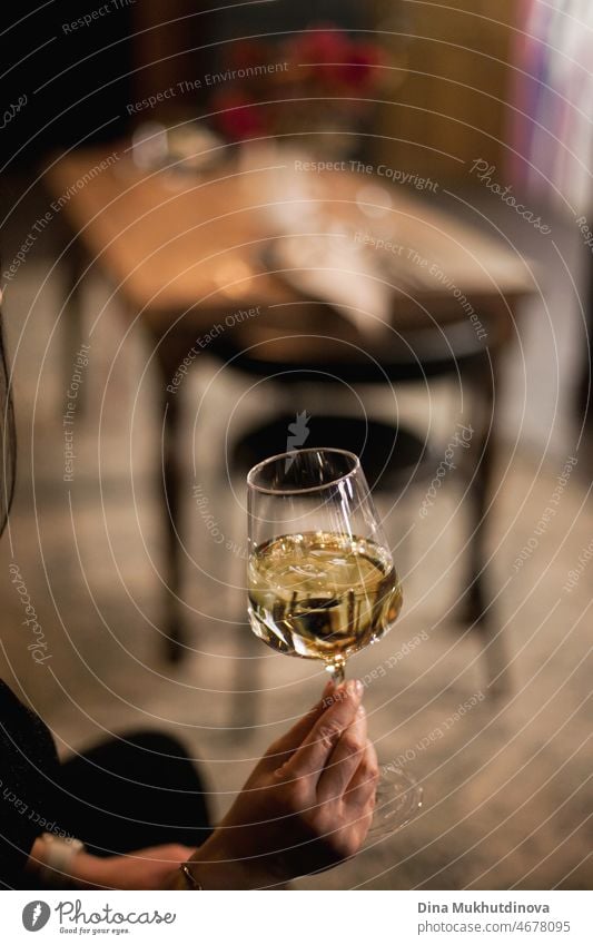 Hand holding a glass of white wine at the bar or restaurant. Drinking wine and celebrating special occasion or holiday. hand celebration background alcohol
