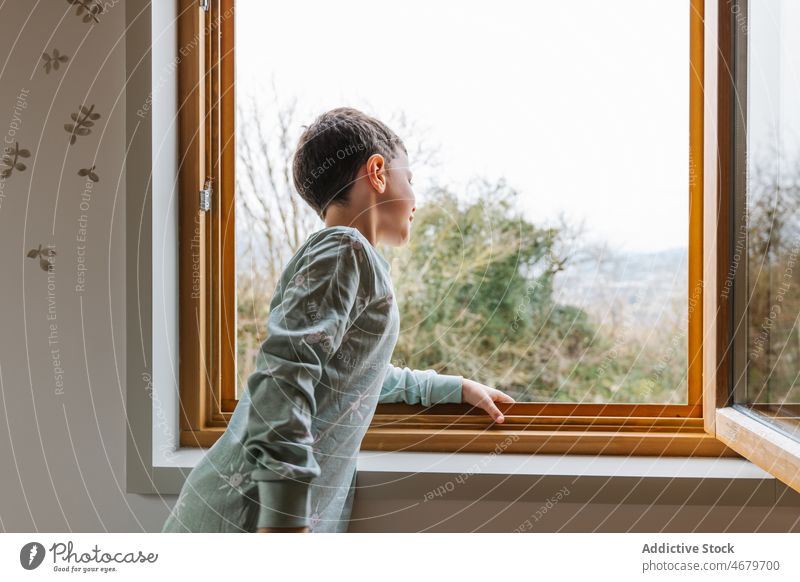 Boy in pajama looking out window boy kid observe interest curious childhood domestic morning apartment adorable flat cute home residential nightwear dwell light