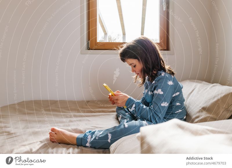Girl in pajama playing on smartphone girl kid childhood bed bedroom videogame pastime morning domestic apartment adorable barefoot flat cute home female