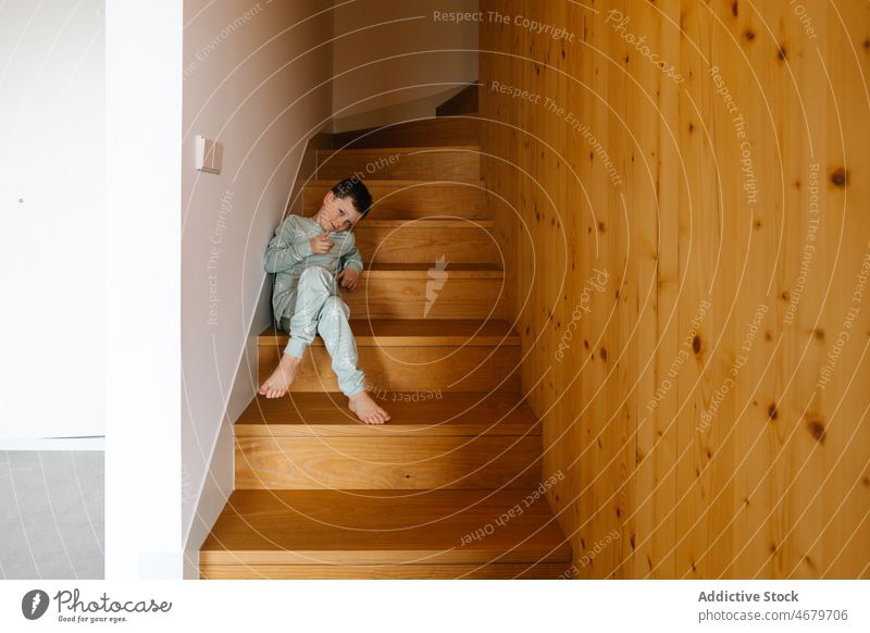 Boy in pajama sitting on stairs boy kid childhood domestic staircase step morning corridor apartment adorable barefoot flat cute home stairway residential